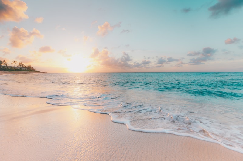 Sunset over the ocean with waves washing onto a sandy shore under a pink and golden sky
