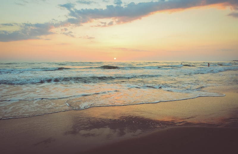 Warm-toned sunset over a calm ocean with gentle waves on a wide sandy beach